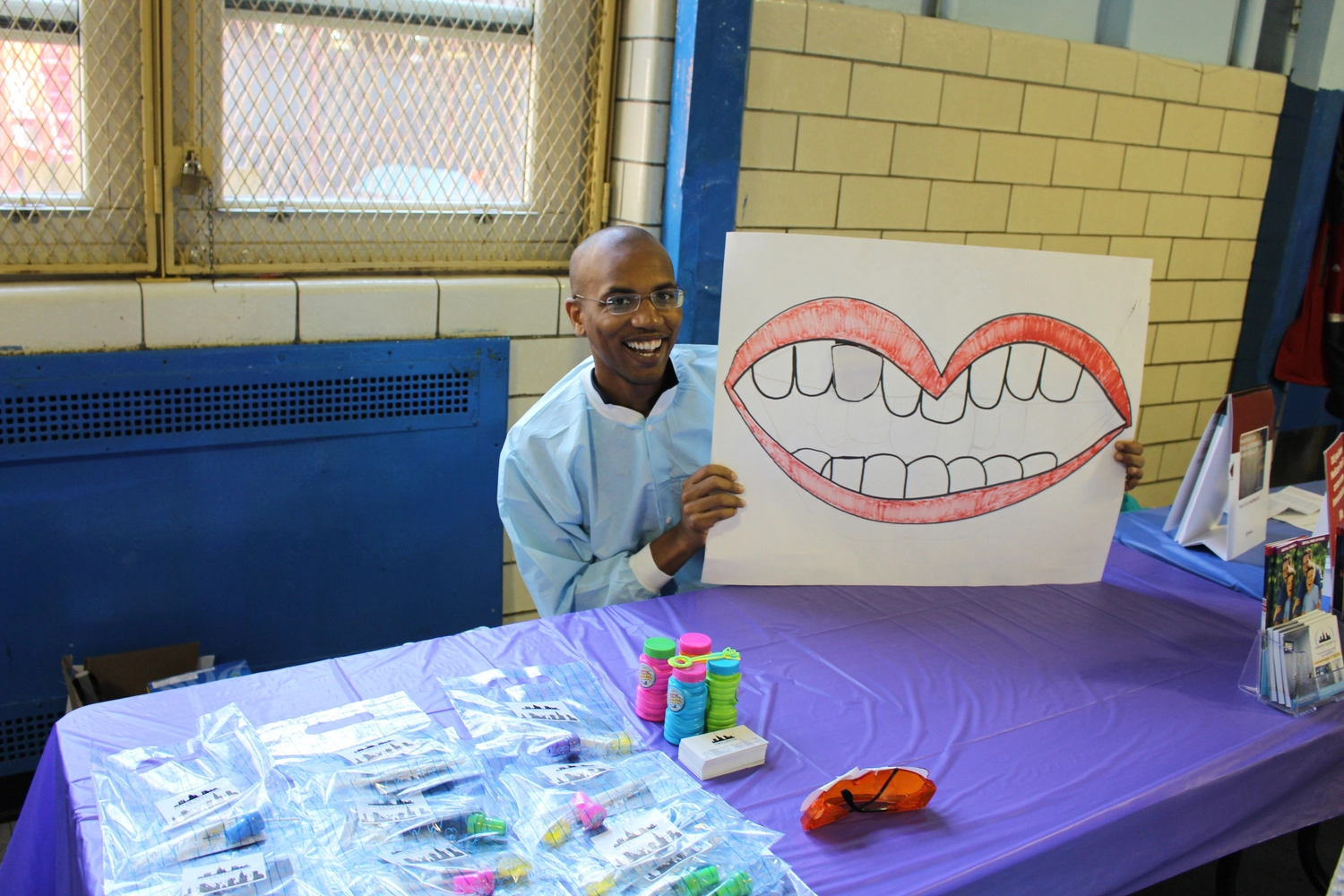 Dr. Shirley holding a large smile poster behind a table of dental goodie bags at a community event