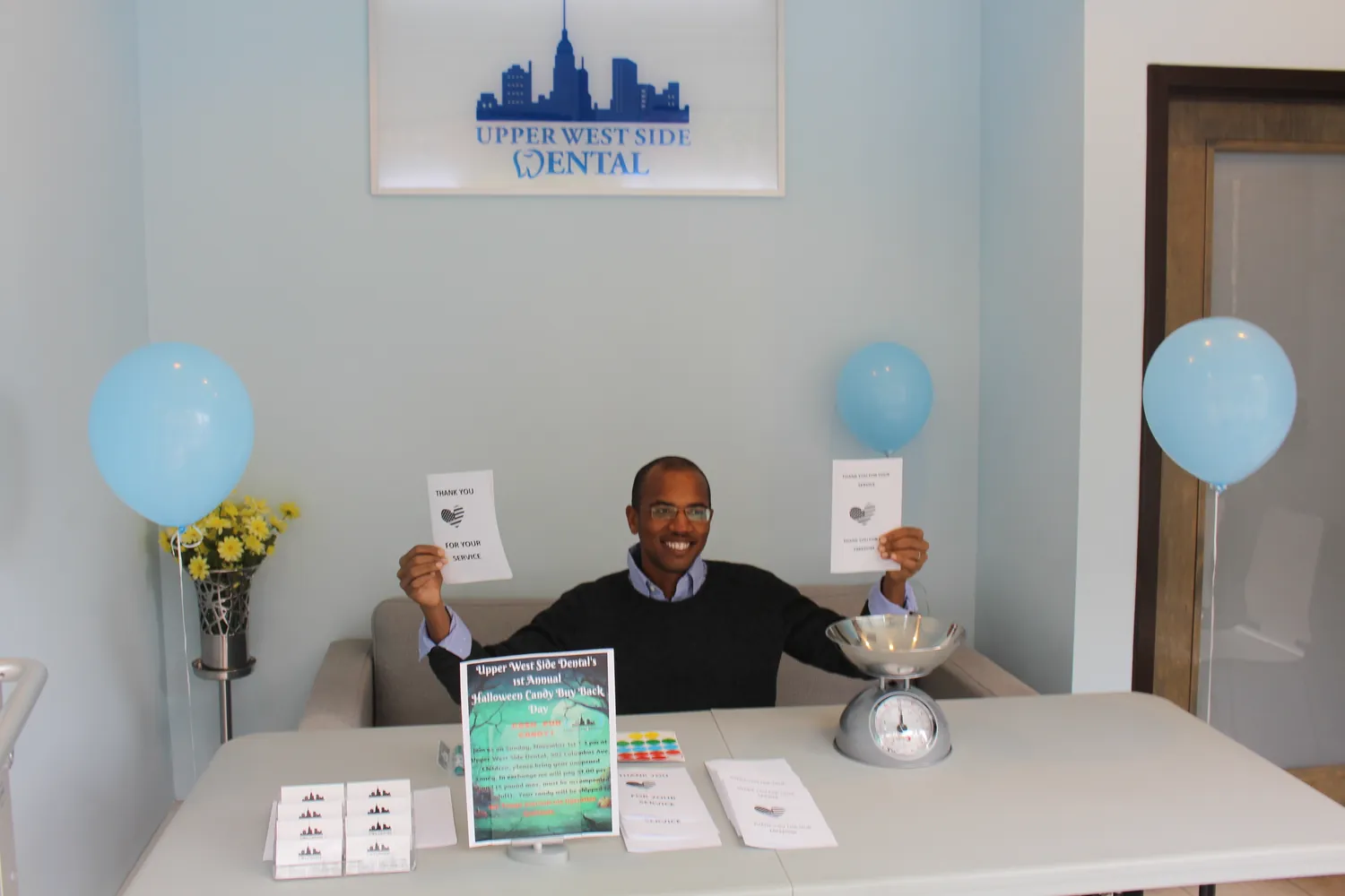 Dr. Shirley holding thank-you cards next to the candy scale at the office Halloween candy buy-back